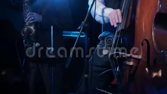 音乐家与萨克斯演奏家在背景特写男艺人在舞台黑暗中演奏木制双低音视频的预览图