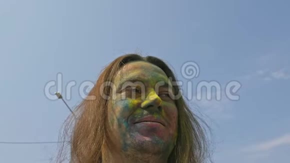 一位年轻的快乐男子头上披着五颜六色的长发白天在冬青节拍自拍视频的预览图