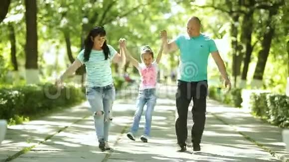 家庭爸爸和妈妈抱着女儿他们在公园里散步笑是微笑的视频的预览图