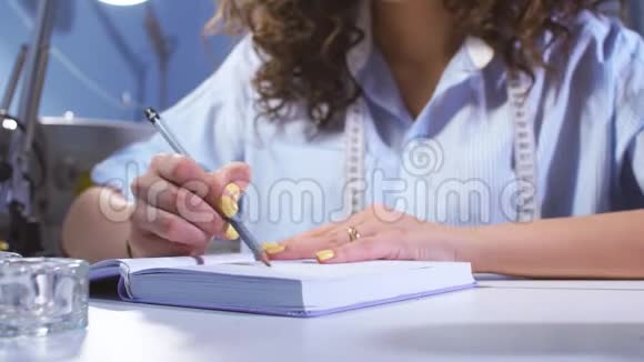 穿蓝色上衣的裁缝在笔记本上写下笔记视频的预览图