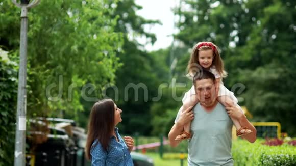 妈妈爸爸和女儿正沿着街走女孩坐在爸爸肩膀上他们笑得很开心视频的预览图