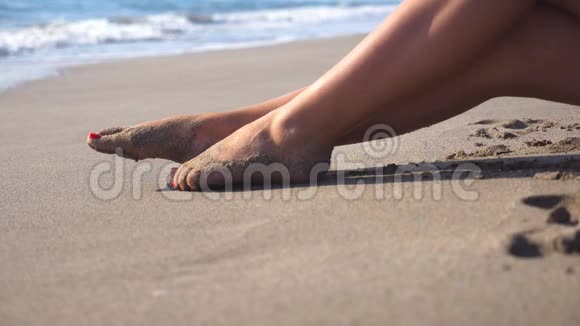 美丽的女性腿躺在沙滩上在海边放松年轻女子坐在海岸上晒黑阳光明媚视频的预览图