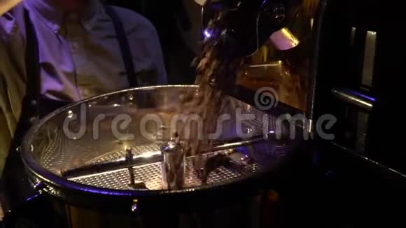 慢动作射击一个穿着黑色围裙和手套的人在咖啡烘焙机上把谷物倒出来视频的预览图