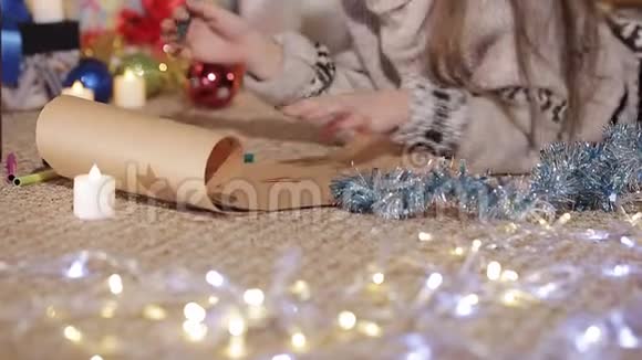一个漂亮的小女孩在一棵装饰精美的圣诞树附近画了一幅圣诞老人的画特写镜头手工艺品视频的预览图