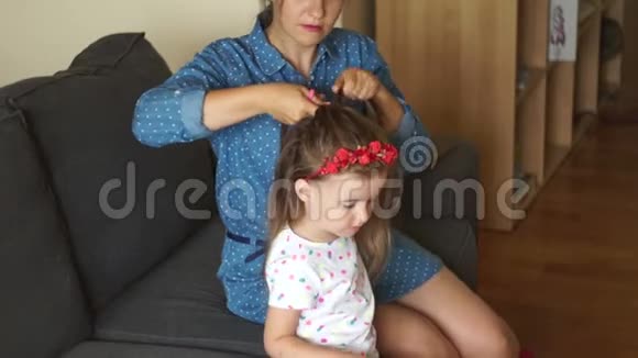年轻的母亲把女儿的头发扎成辫子一个幸福的家庭母亲节妇女节视频的预览图