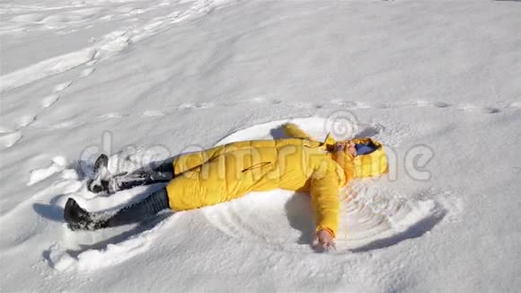 快乐的年轻女人躺在地上做雪天使在干净的白色表面上穿黄色夹克的女孩视频的预览图