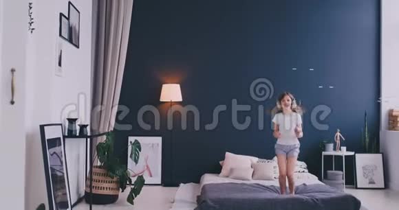 一个小女孩的肖像带着耳机听音乐在父母的床上跳舞概念音乐视频的预览图