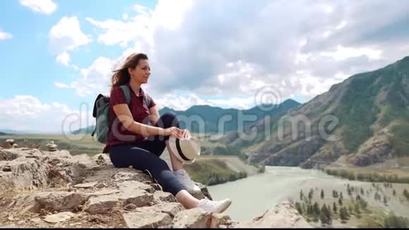 一个女孩在山里旅行的肖像坐在悬崖边上的岩石上休息的年轻女子视频的预览图