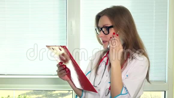 美丽的年轻医生带着文件夹和她的病人在电话里交谈视频的预览图