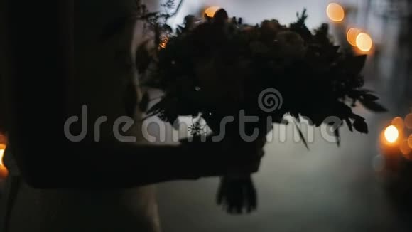 新娘手中的婚礼花束在室内在背景上点燃蜡烛新娘手里捧着漂亮的婚礼花束视频的预览图
