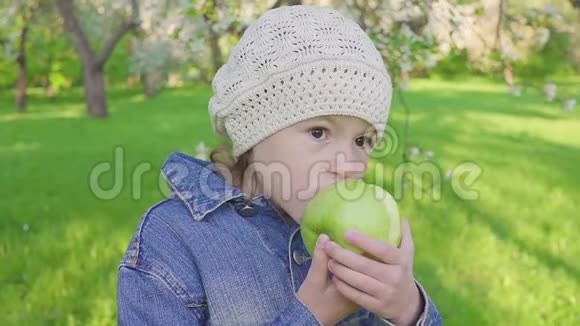 小女孩肖像吃绿苹果户外花圃背景上有苹果的女孩视频的预览图