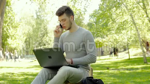 学生打电话在公园里用笔记本电脑工作视频的预览图