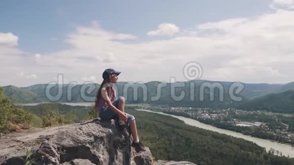 小童旅行者欣赏坐在岩石上的风景山里的女游客视频的预览图