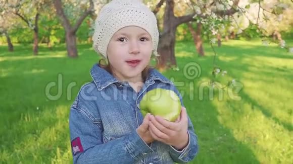 小女孩肖像吃绿苹果户外花圃背景上有苹果的女孩视频的预览图