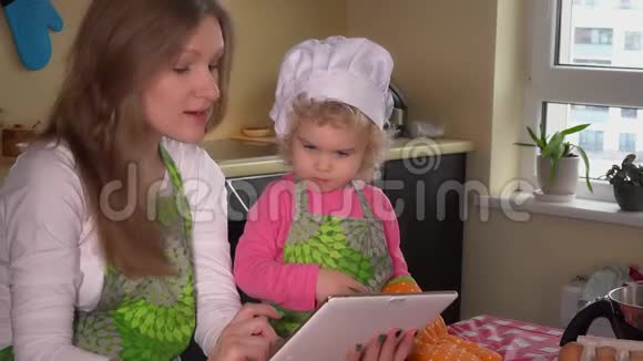 可爱的家庭女孩带着平板电脑在网上寻找蛋糕配方视频的预览图