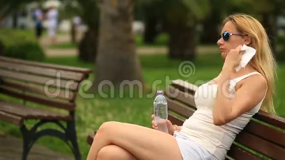 女人坐在城市公园的长凳上因炎热而精疲力竭视频的预览图