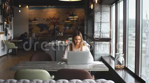 女商人坐在窗边的咖啡馆里用笔记本电脑打字视频的预览图