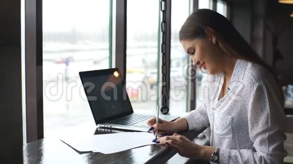 一个迷人的年轻学生坐在一家带笔记本电脑的咖啡店里看着文件视频的预览图