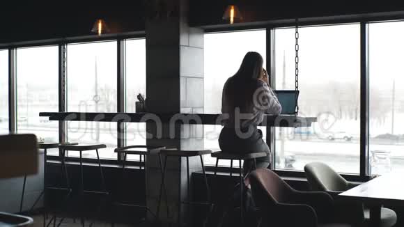 可爱的年轻女经理在大窗户附近用笔记本电脑工作视频的预览图