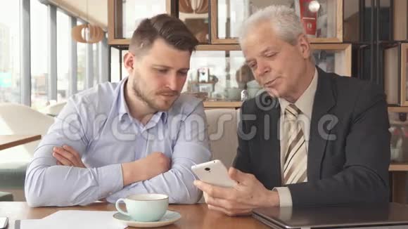 高级商人在他的智能手机上向他的伴侣展示一些东西视频的预览图