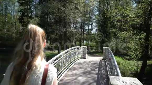 这位留着一头长发的年轻女子在夏季花园的桥上散步视频的预览图