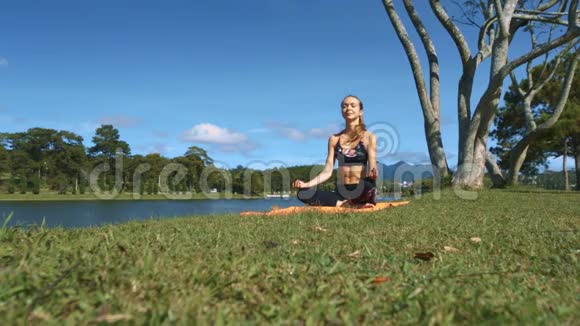 女孩坐在河边绿草上的瑜伽姿势视频的预览图