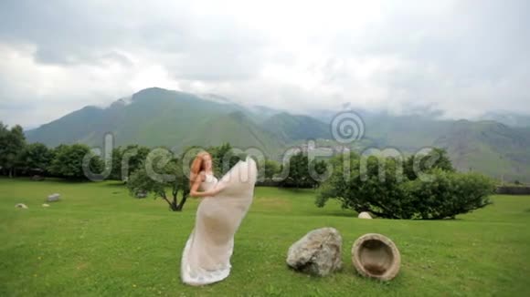 美丽的红发新娘在群山的背景下跳舞慢动作视频的预览图
