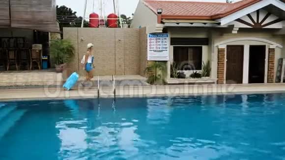 戴着帽子的金发女孩穿着蓝色包的工作服住在一家带游泳池的热带酒店里4K视频的预览图
