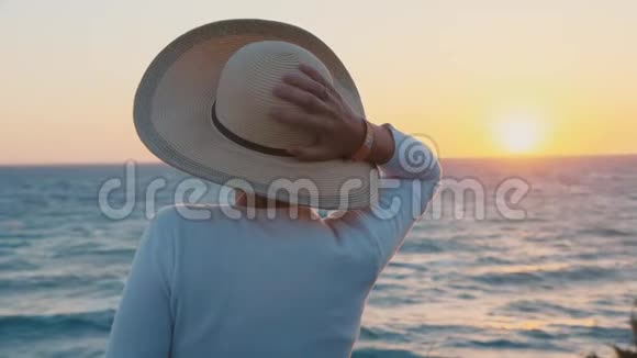 戴着帽子的女孩看着大海中的日落视频的预览图