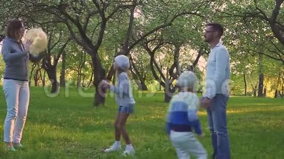 父母和两个女儿在盛开的花园里的春天公园里玩球积极的休闲视频的预览图