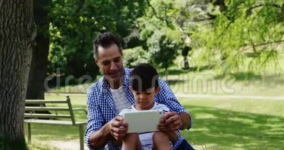 男孩坐在父亲的膝上用数码平板电脑视频的预览图