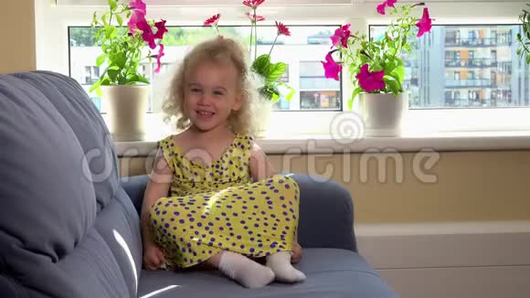 可爱的情绪蹒跚学步的女孩穿着黄色连衣裙坐在沙发上表现出情感视频的预览图