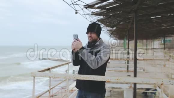 年轻的高加索人在风暴中的海上智能手机上拍照视频的预览图
