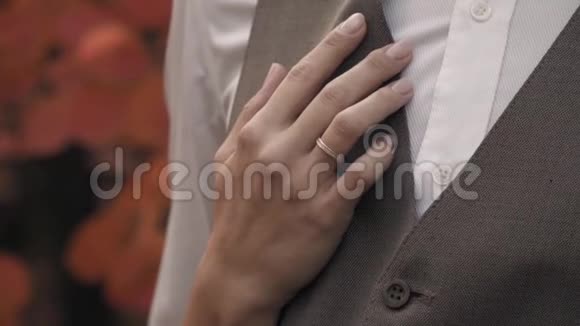 一只戴着订婚戒指的女性手在秋天公园的背景下拥抱一个穿西装的男人视频的预览图