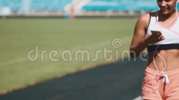 一个穿着运动服的强壮女孩在体育场奔跑的肖像美丽的女孩在体育场奔跑倾听视频的预览图