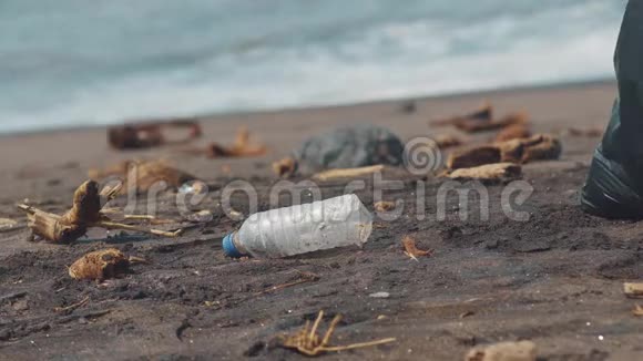 特写志愿者拿起塑料瓶在黑色沙滩上放入黑色塑料袋志愿者打扫卫生视频的预览图