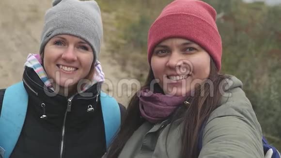 两个穿着帽子和夹克的快乐女孩做自拍看着相机挥手慢速运动高清1920x1080视频的预览图