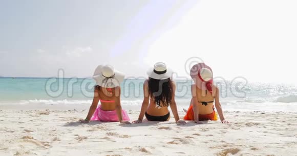 三个穿比基尼和草帽的女孩在海滩上的后景享受日光浴女游客在暑假成群结队视频的预览图