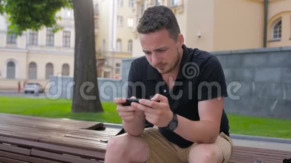 坐在长凳上玩智能手机的快乐年轻人视频的预览图