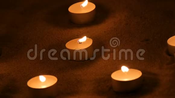 许多美丽的圆形的白色的小蜡烛在黑暗的沙子里燃烧视频的预览图