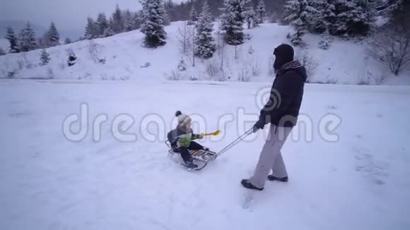 年轻的幸福家庭在雪林里玩得很开心父亲把他的小儿子卷在雪橇上晚上散步爸爸和爸爸视频的预览图