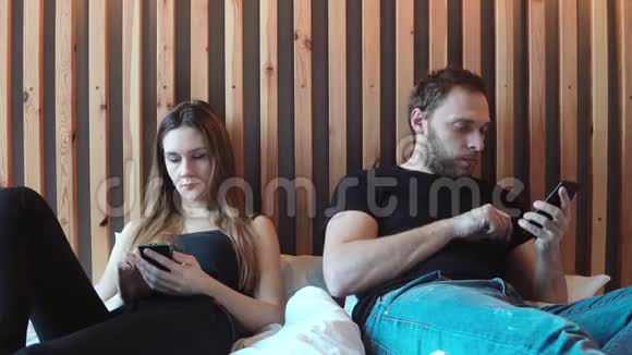 夫妻俩坐在床上不说话在智能手机上打字年轻人和女人吵架视频的预览图