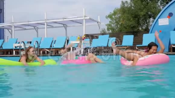 在游泳池边的充气圈和床垫上游泳的快乐女孩穿泳衣的漂亮女朋友在夏天休息视频的预览图