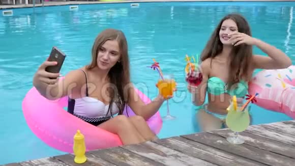 充气戒指上的漂亮女友在泳池里自拍穿着泳衣的女孩手拿鸡尾酒拍照视频的预览图