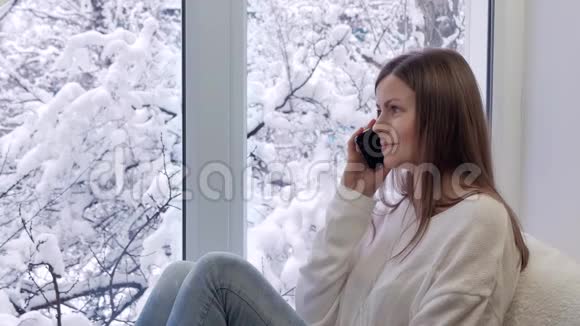 坐在窗台上用智能手机说话的漂亮女孩冬天在外面视频的预览图
