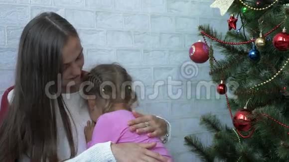 年轻的母亲抱着她哭泣的小女儿在圣诞树旁视频的预览图