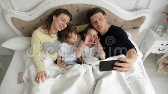 有趣的家庭是一起躺在床上拍照母亲父亲和玩耍的孩子在利用自我视频的预览图