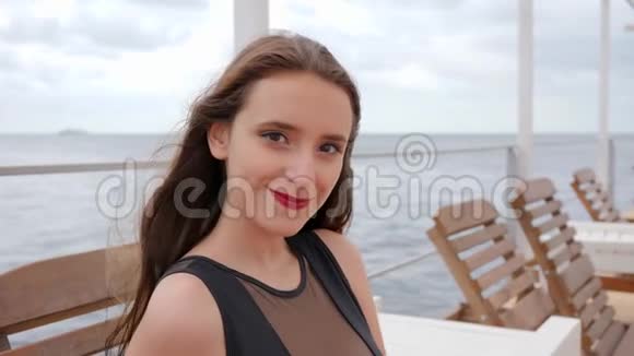 穿着泳衣的年轻女子坐在躺椅上微笑着风吹起头发女的在海边看着镜头视频的预览图