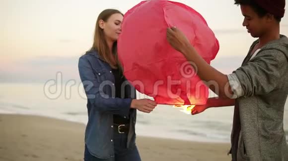 年轻的多民族夫妇在发射前手持红纸灯笼在海滩上浪漫的约会有魅力的女人视频的预览图