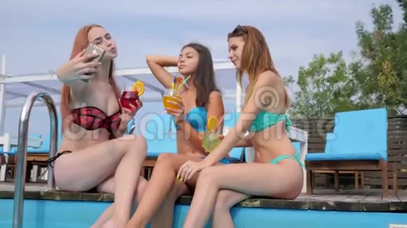 年轻女性在游泳池附近的避暑胜地上录制视频女友的图片电话视频的预览图